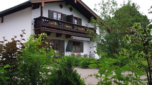 Ein zweistöckiges Gebäude mit einem Blumen geschmückten Balkon, umgeben von üppiger Vegetation.
