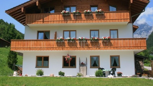 A two-story wooden chalet with balconies, a white facade, and a mountain backdrop.