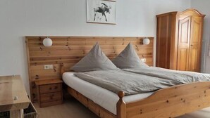A wooden bed with two pillows, a bedside table, and a wardrobe in a room with a simple design.