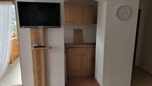 A compact kitchen with wooden cabinets, a built-in TV, and a clock on the wall.