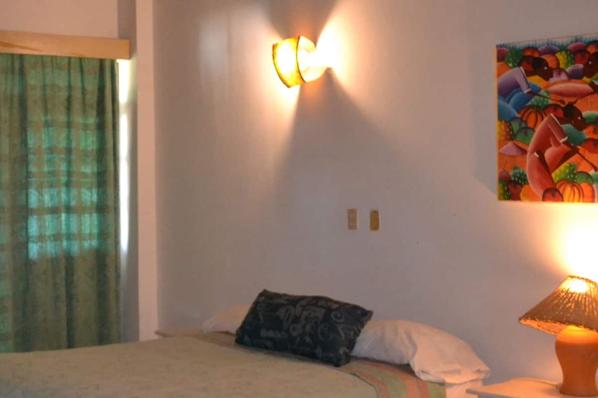 A bedroom with a bed, a nightstand, a lamp, a wall-mounted light, and a painting.