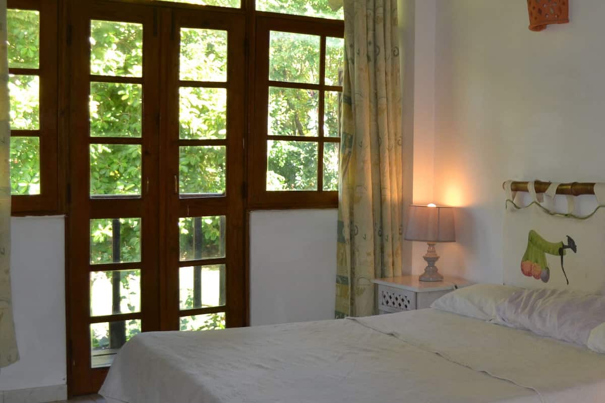 A bedroom with a bed, two bedside lamps, a window with curtains, and a wall with a decorative headboard.