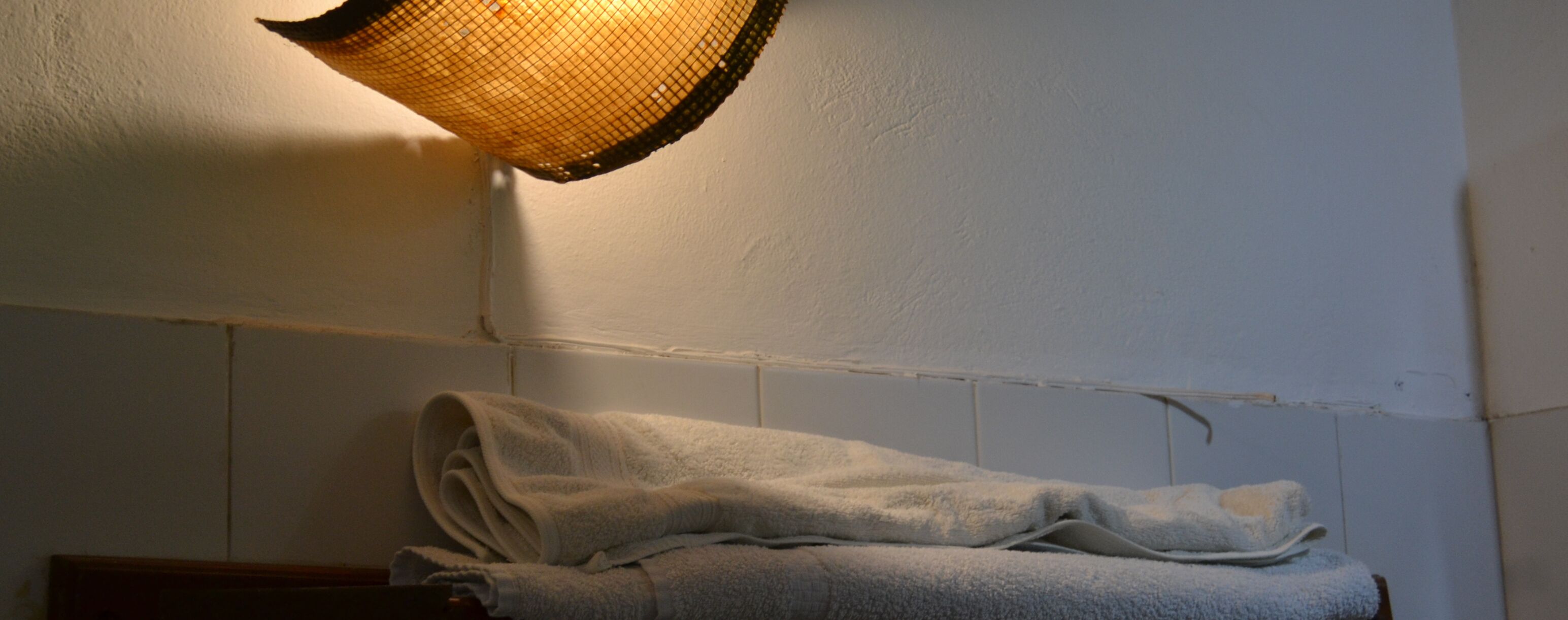 A bathroom with a towel rack holding folded towels, a textured wall, and a hanging light fixture.
