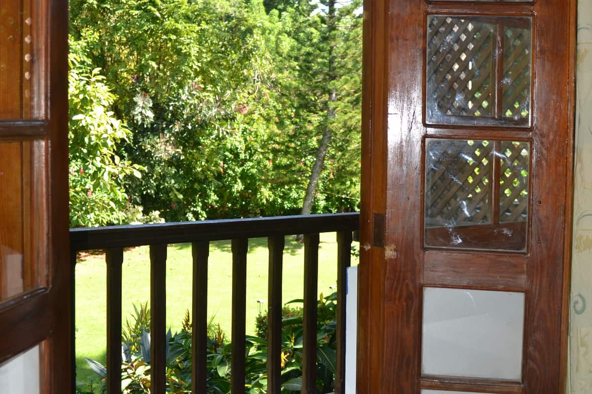A wooden door with glass panels, leading to a balcony with a metal railing and a view of a garden with trees and grass.