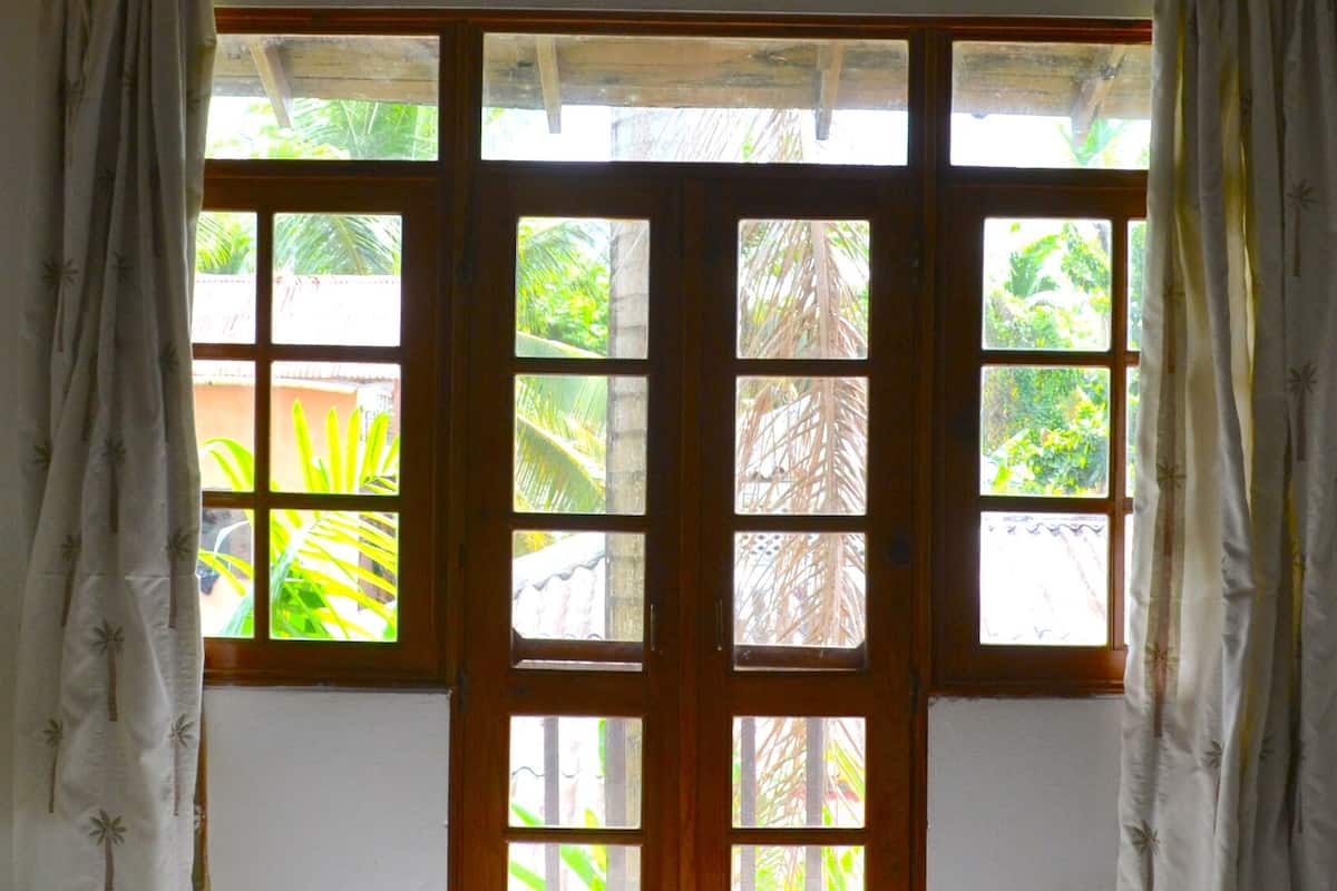 A room with a wooden-framed window with multiple panes, white curtains, and a lamp on a table.