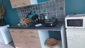 A compact kitchen with a black countertop, a stove, a microwave, and a sink. There are cabinets and a small basket on the counter. - Studio nono (Pointe-à-Pitre)