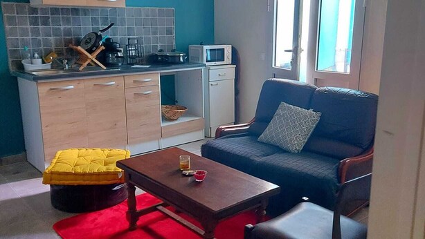 A compact living space with a kitchenette, a sofa, a dining table, and a red rug. - Studio nono (Pointe-à-Pitre)