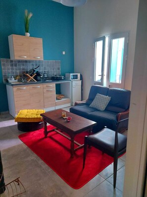 A compact living space with a kitchenette, a sofa, a dining table, and a red rug. - Studio nono (Pointe-à-Pitre)