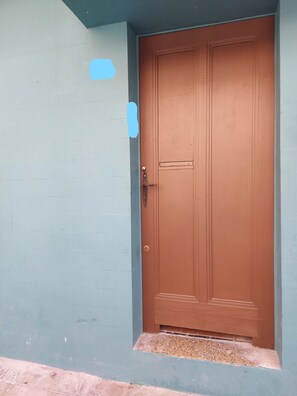 A brown door with a keyhole and a handle, set in a light blue wall with a small step leading up to it.