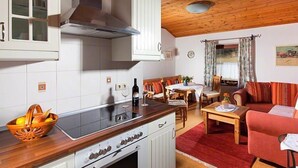 Een compacte keuken met witte kastjes, een fornuis en een zithoek met een rode bank en houten tafel.