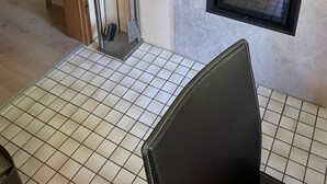 A room with a tiled floor, a fireplace, framed pictures on the wall, and a door leading to another room.