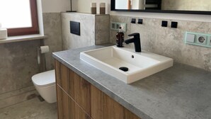 A modern bathroom with a white sink, black faucet, and a mirror above it. There is a toilet to the left and a window above it.
