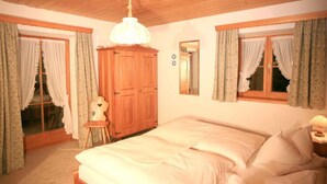 Une chambre avec un grand lit, une armoire en bois et deux fenêtres avec des rideaux.