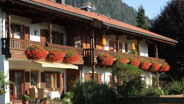 Un bâtiment à deux étages doté d’un balcon, de volets en bois et de fleurs rouges.