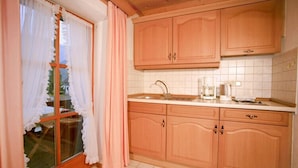 A kitchen with wooden cabinets, a sink, and a window with curtains. - Apartment 4 for 2 persons with balcony, 27 sqm, kitchen, living room/bedroom (Inzell)