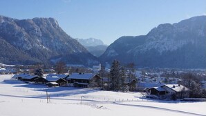 Un villaggio innevato con case in legno tradizionali, cielo sereno e montagne sullo sfondo.
