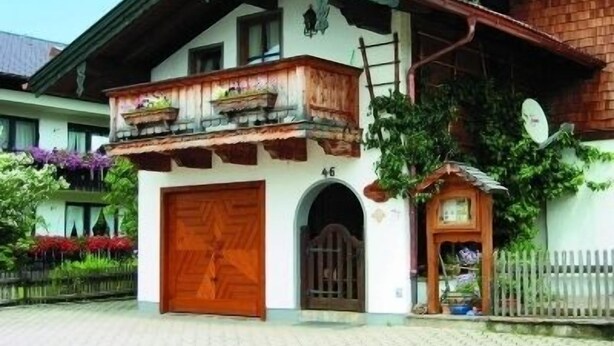 Ein traditionelles Chalet mit Holzbalkon, einer großen Holztür und einem kleinen Garten mit Blumen.
