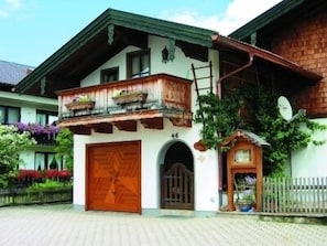 A traditional chalet with a wooden balcony, a large wooden door, and a small garden area with flowers. - Vacation apartment 2 for 4 persons, 2 bedrooms, balcony, 78 sqm (Inzell)