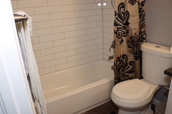 A bathroom with a white bathtub, a toilet, and a shower curtain with a floral pattern. - Cheerful, Newly furnished 3 bdrm home with indoor fireplace. (Aurora)