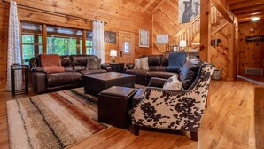 L’intérieur chaleureux d’un chalet avec un canapé en cuir, un fauteuil à motifs et une table basse en bois.