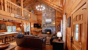 Un intérieur de chalet chaleureux avec une cheminée en pierre, des murs en bois, un coin bar et un espace salon confortable.