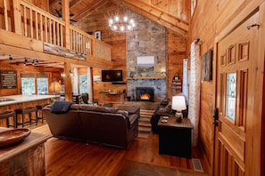 A cozy cabin interior with a stone fireplace, wooden walls, a bar area, and a comfortable seating arrangement.