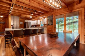 A wooden cabin interior with a kitchen, dining area, and large windows.