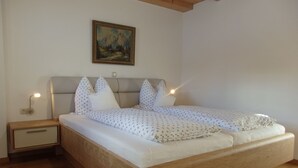A bedroom with a wooden bed, a nightstand, a wall-mounted lamp, and a painting above the bed. - Ferienwohnung Jenner 48 qm, für 2 Personen, Balkon, 1 Schlafzimmer (Schönau am Königssee)