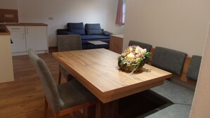 A dining area with a wooden table, grey upholstered chairs, and a centerpiece with flowers and candles. - Ferienwohnung Jenner 48 qm, für 2 Personen, Balkon, 1 Schlafzimmer (Schönau am Königssee)