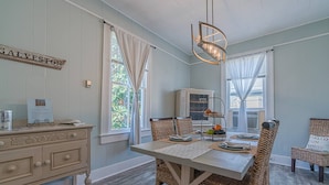 A dining area with a white table, wicker chairs, a chandelier, and a cabinet with a sign reading "GALVESTON". - Walk to Beach & UTMB |Dogs Ok |Game Room (Galveston)