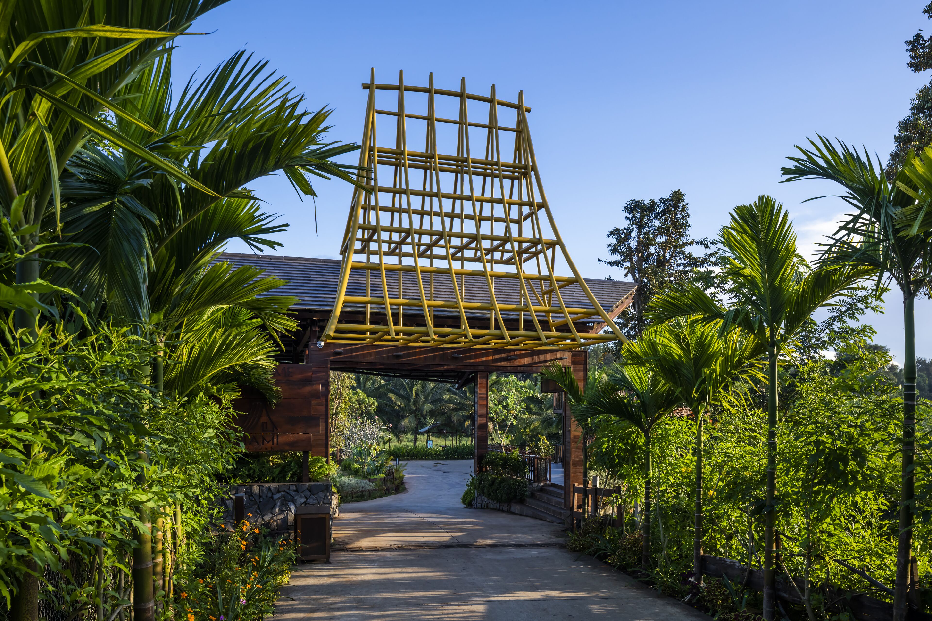 Una estructura de pérgola de madera con techo inclinado, rodeada de abundante vegetación y palmeras.