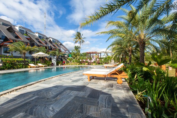 A swimming pool with lounge chairs, palm trees, and a building with a sloped roof. - Hami Garden (Tan An)