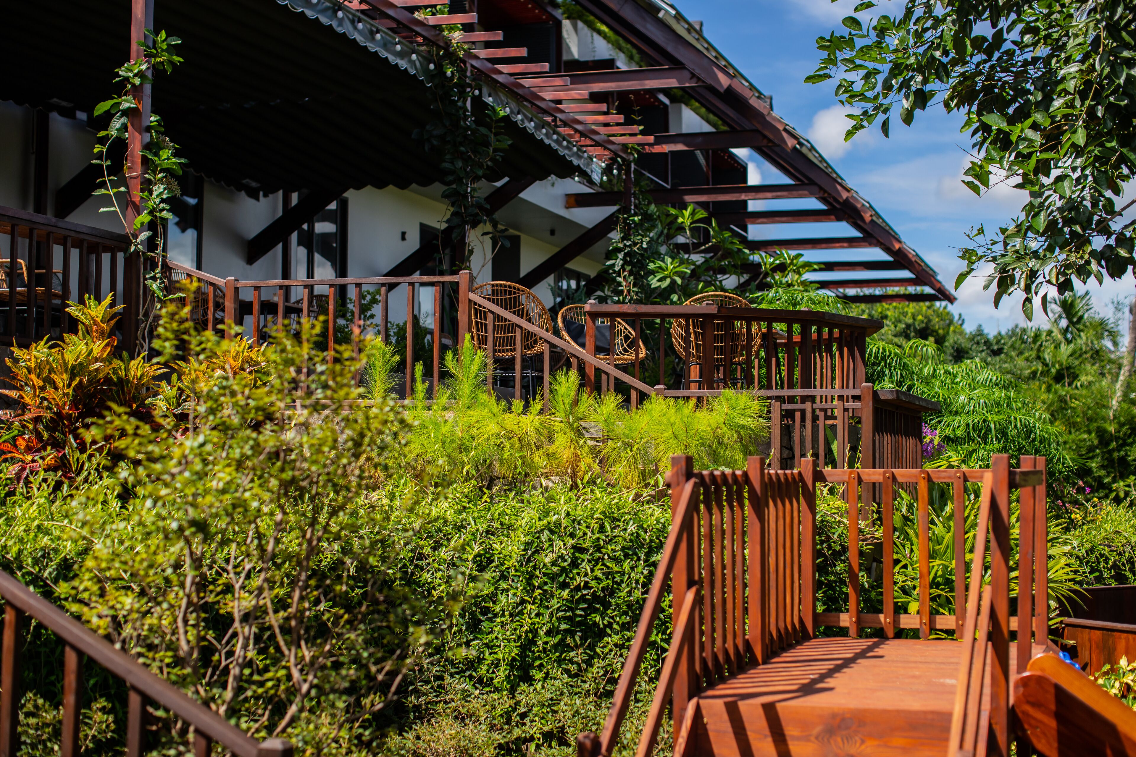 A wooden staircase leading to a building with a traditional design, surrounded by lush greenery.