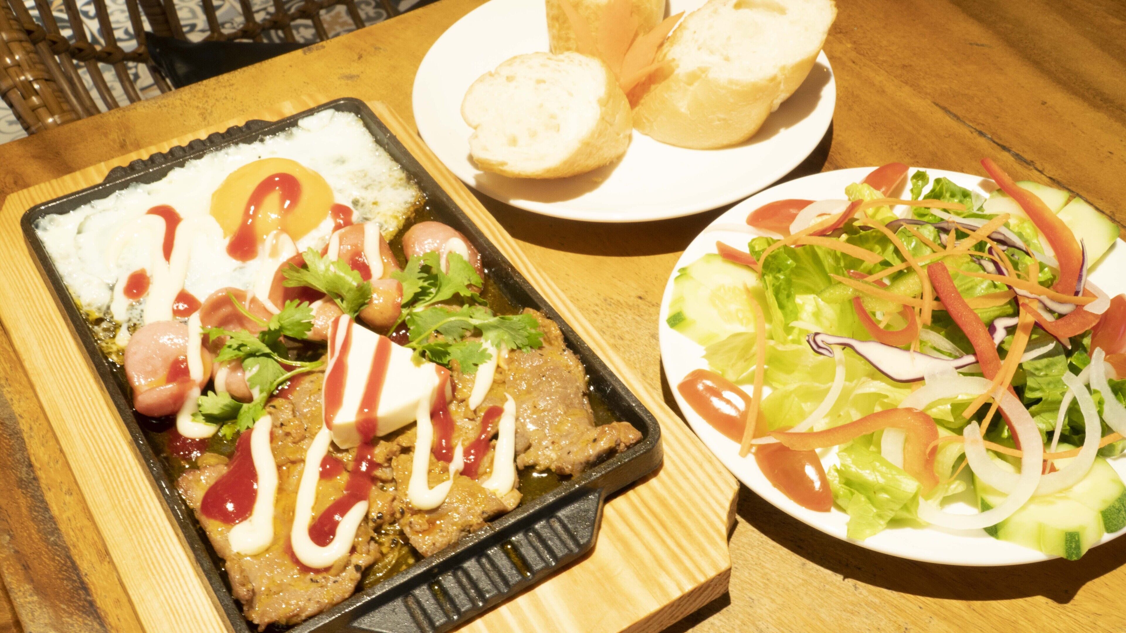 Een maaltijd bestaande uit een braadpan met vlees en groenten, een broodbord en een salade met verschillende groenten.