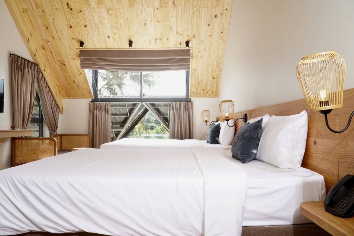 Une chambre avec un grand lit, un plafond en bois et une vue sur les palmiers par la fenêtre.
