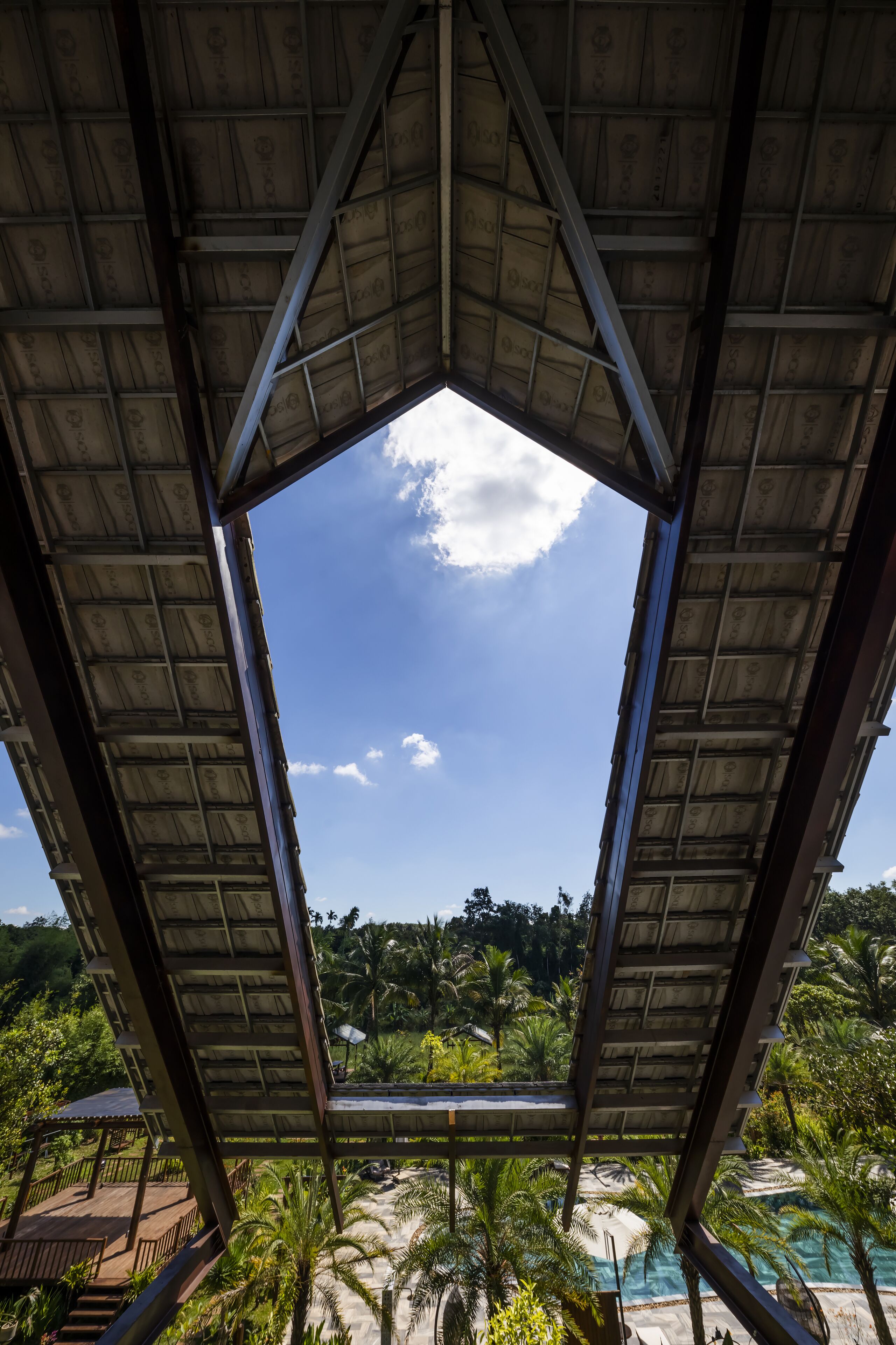 A view through a geometric structure with a pool and palm trees in the background.