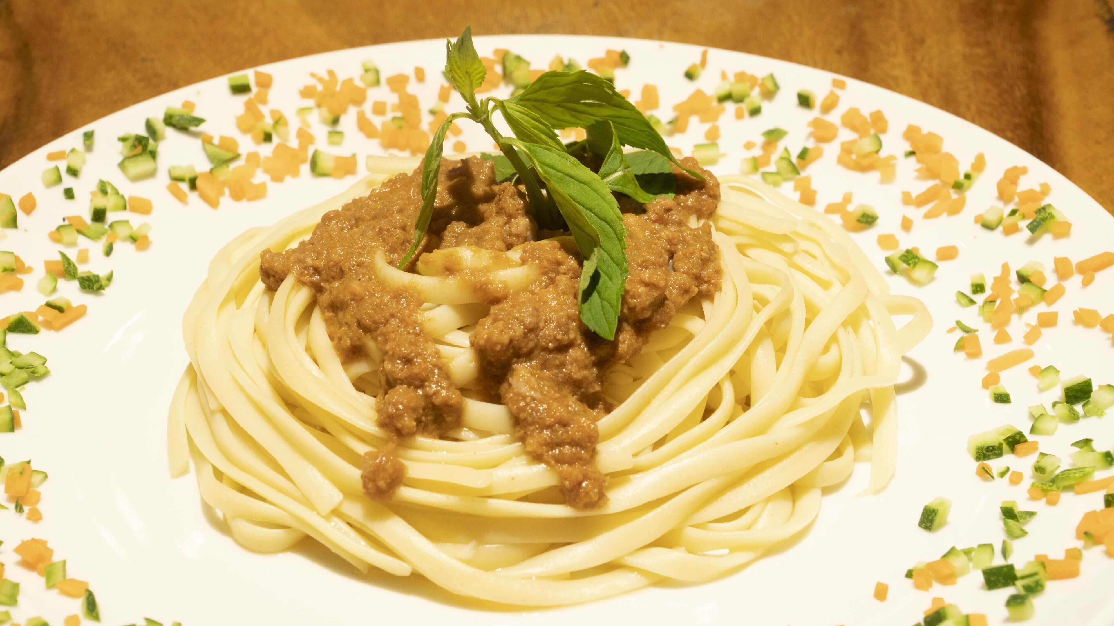 A plate of spaghetti with meat sauce and garnished with basil leaves.