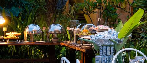 An outdoor buffet setup with various food items and beverages, surrounded by lush greenery.