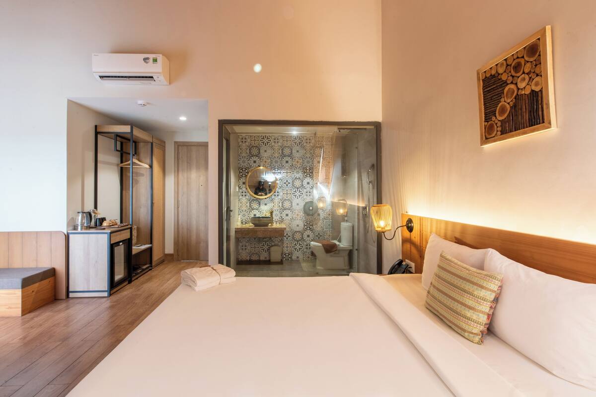Une chambre d’hôtel avec un lit, une table de chevet et une salle de bain visible à travers une porte ouverte.
