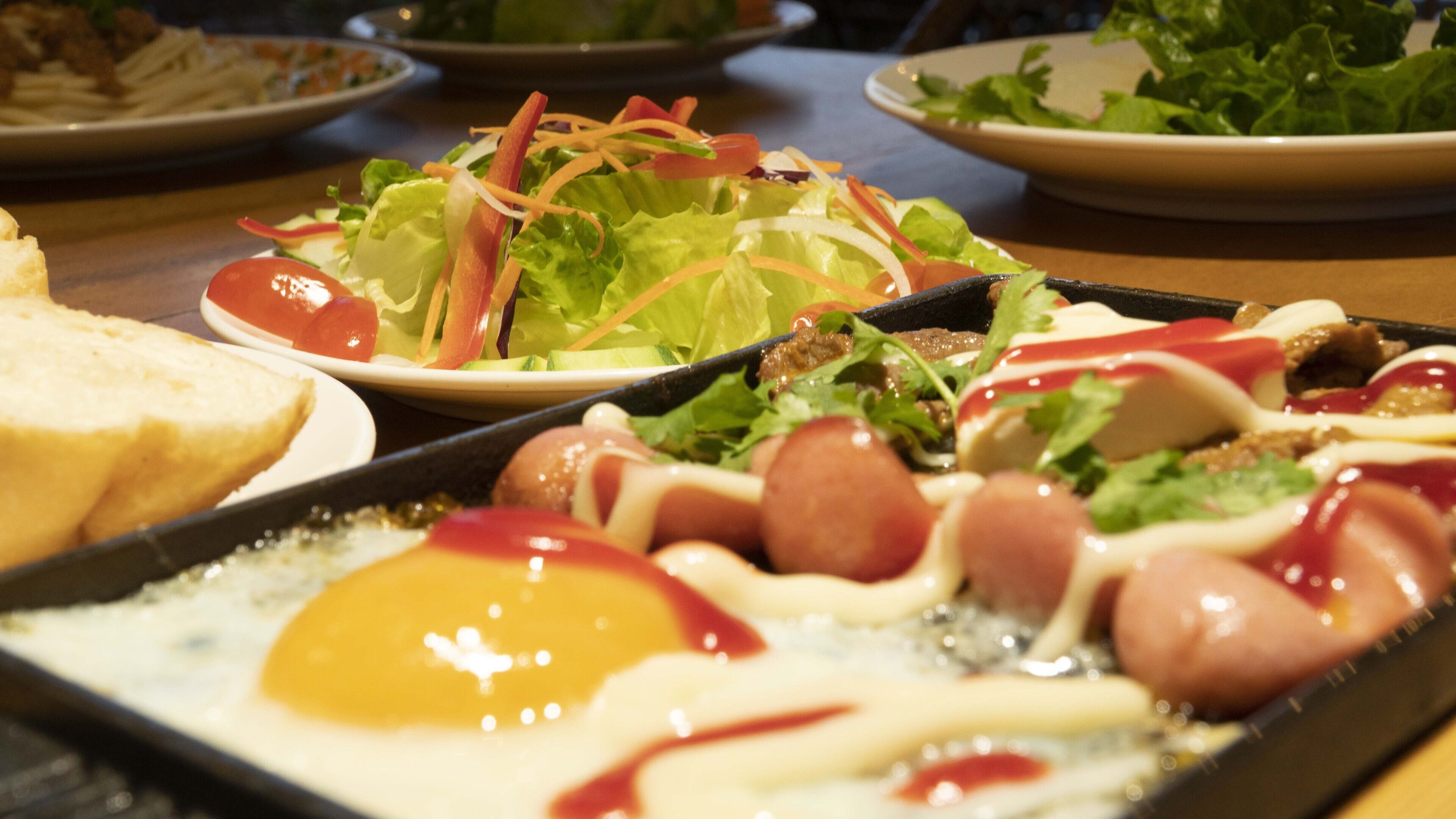 Un assortiment de plats comprenant une salade, du pain et une assiette de saucisses et d’œufs.