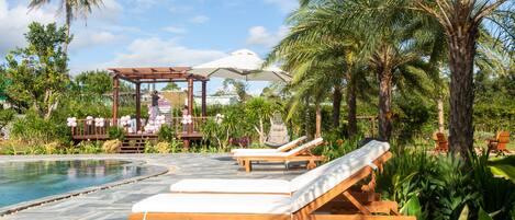 Ein Poolbereich mit Liegestühlen und einer Pergola mit Sonnenschirmen.