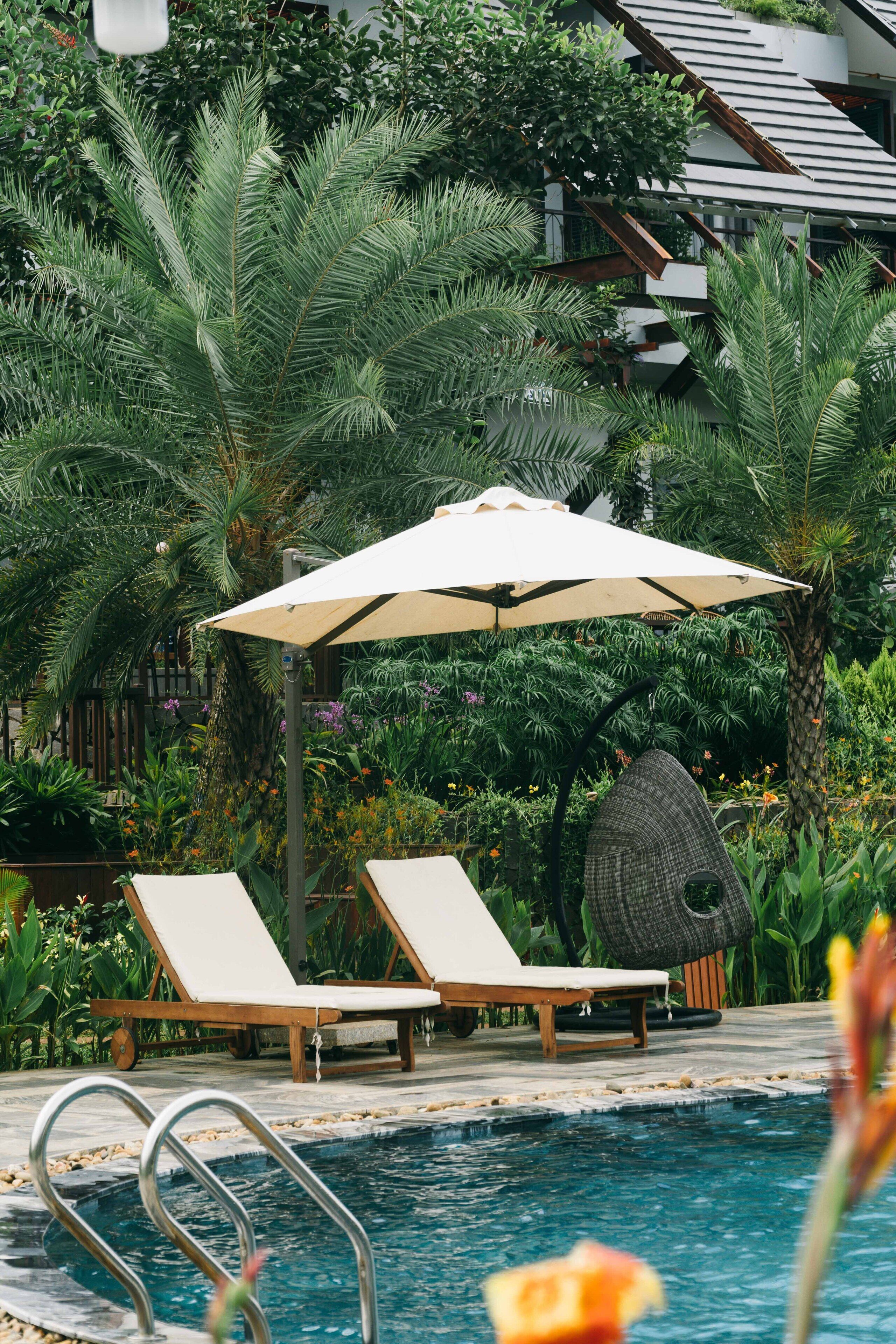 A pool area with lounge chairs and an umbrella, surrounded by lush greenery.