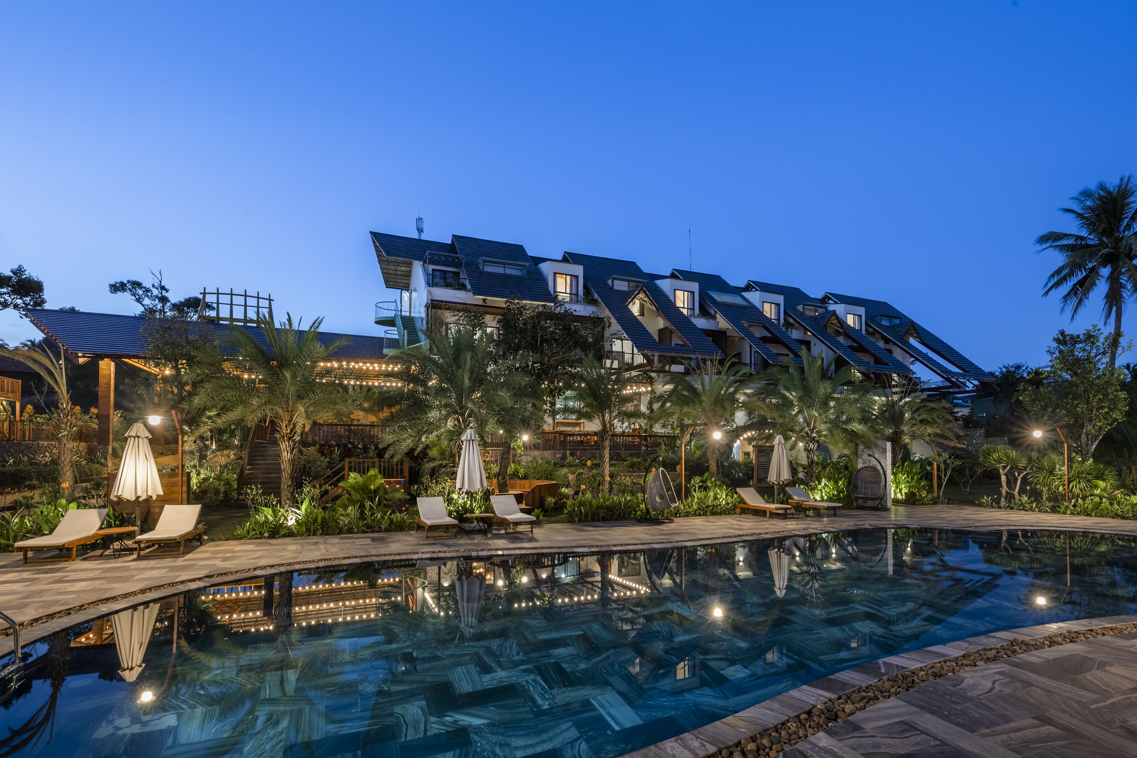 A modern hotel with a rooftop pool area, lounge chairs, and palm trees.