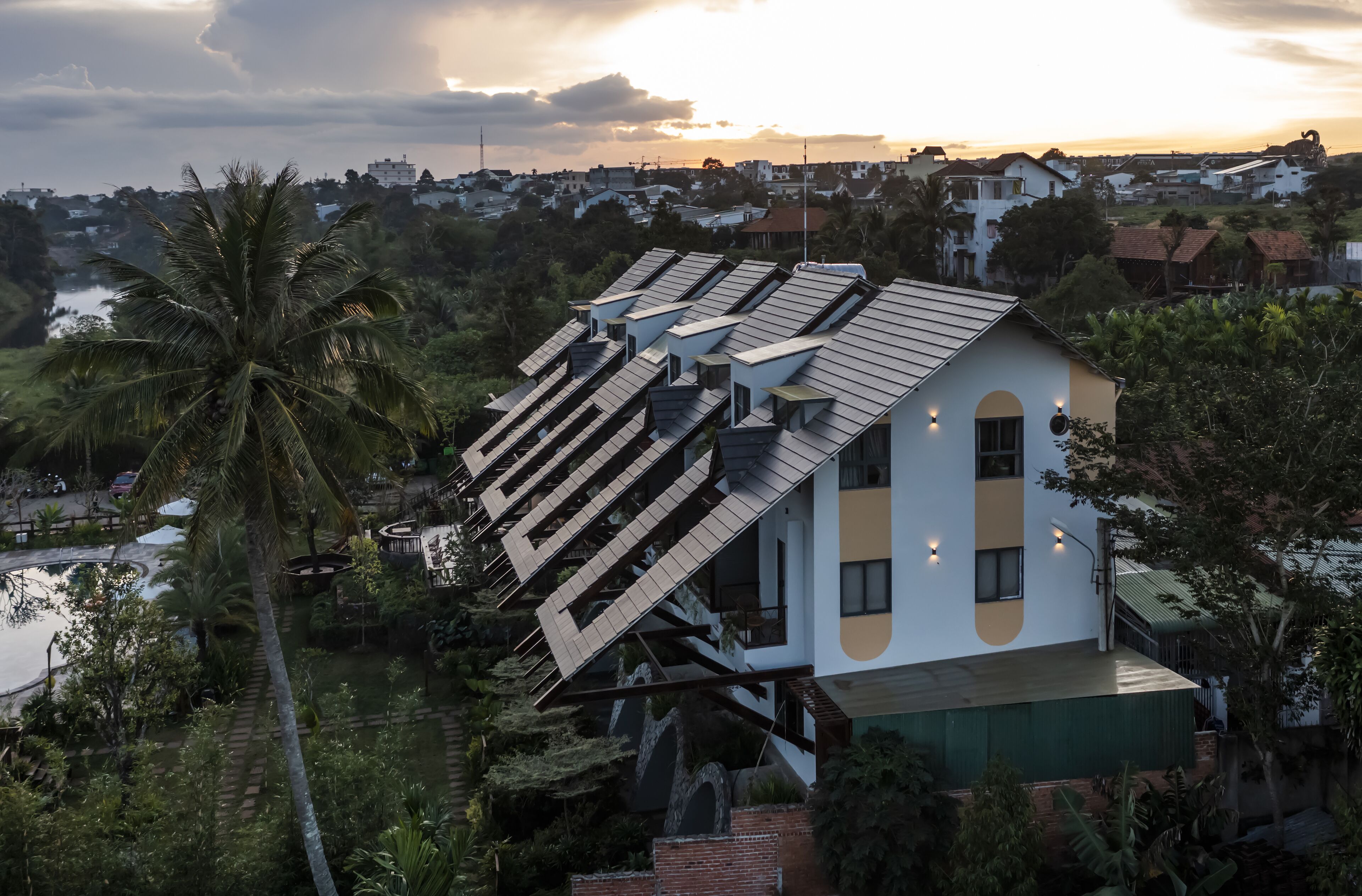 Et moderne hus med skråt tag, omgivet af frodig vegetation og et vandareal.