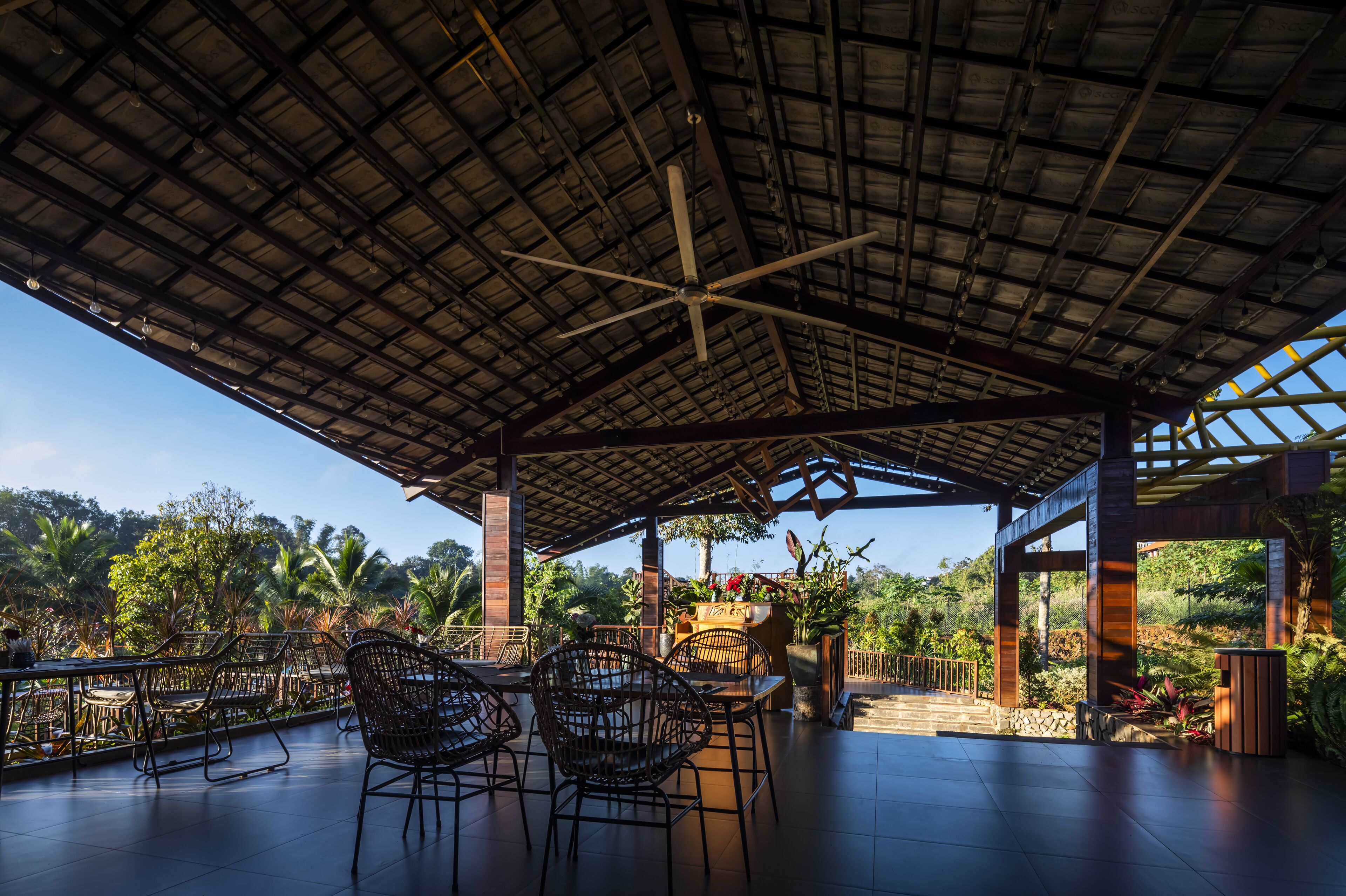 An outdoor patio area with a covered roof, wicker furniture, and a view of the surrounding greenery.
