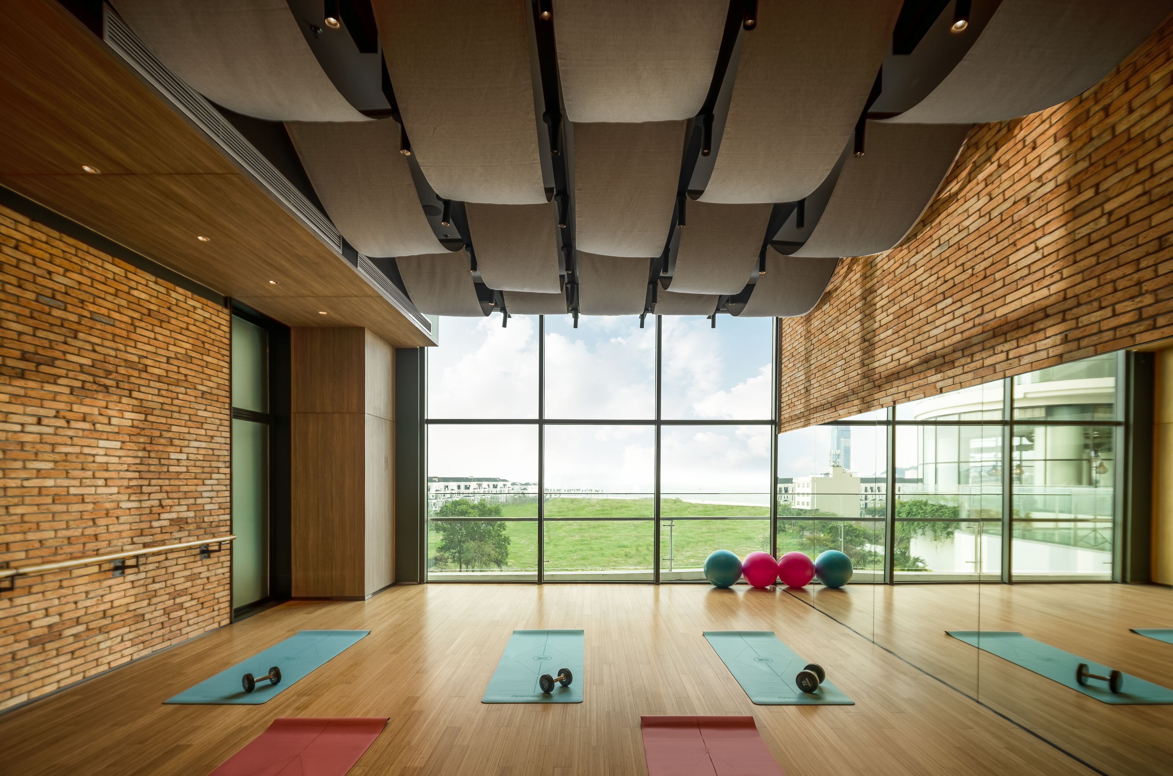 A spacious gym with large windows, wooden floors, and exercise mats.