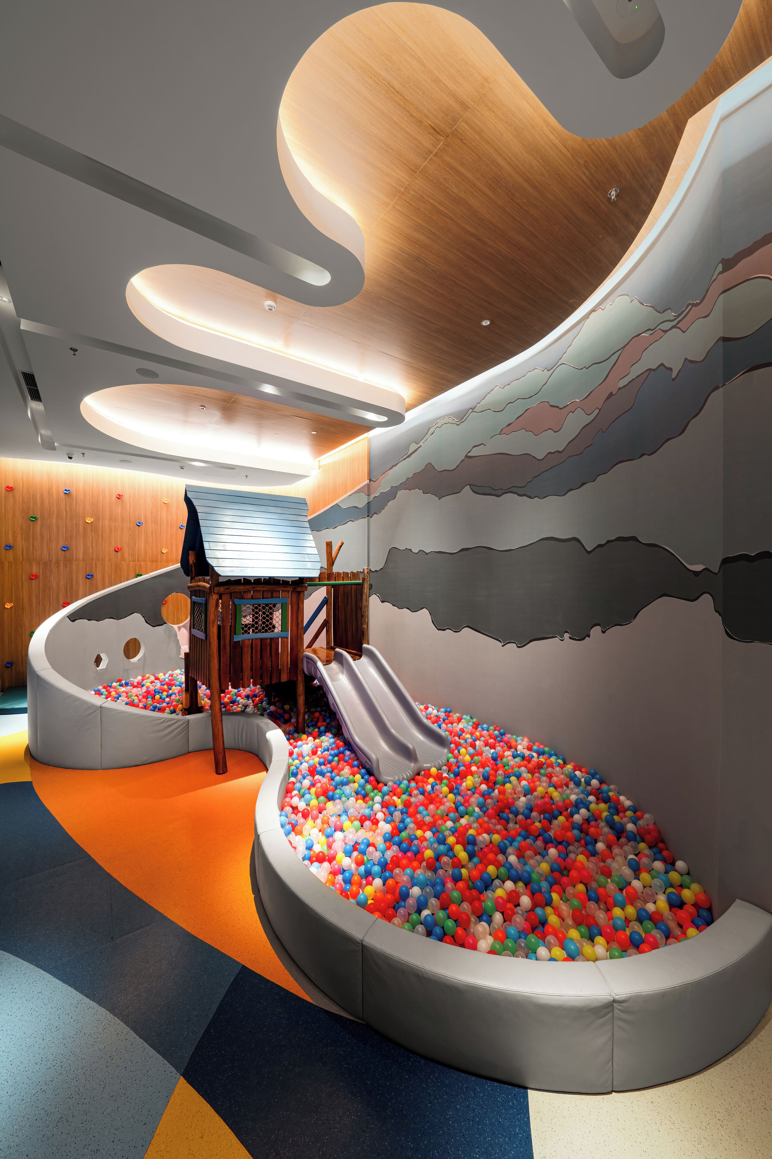 A play area with a slide, ball pit, climbing wall, and soft seating.
