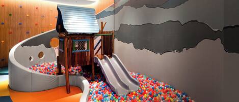 A play area with a slide, ball pit, climbing wall, and soft seating.