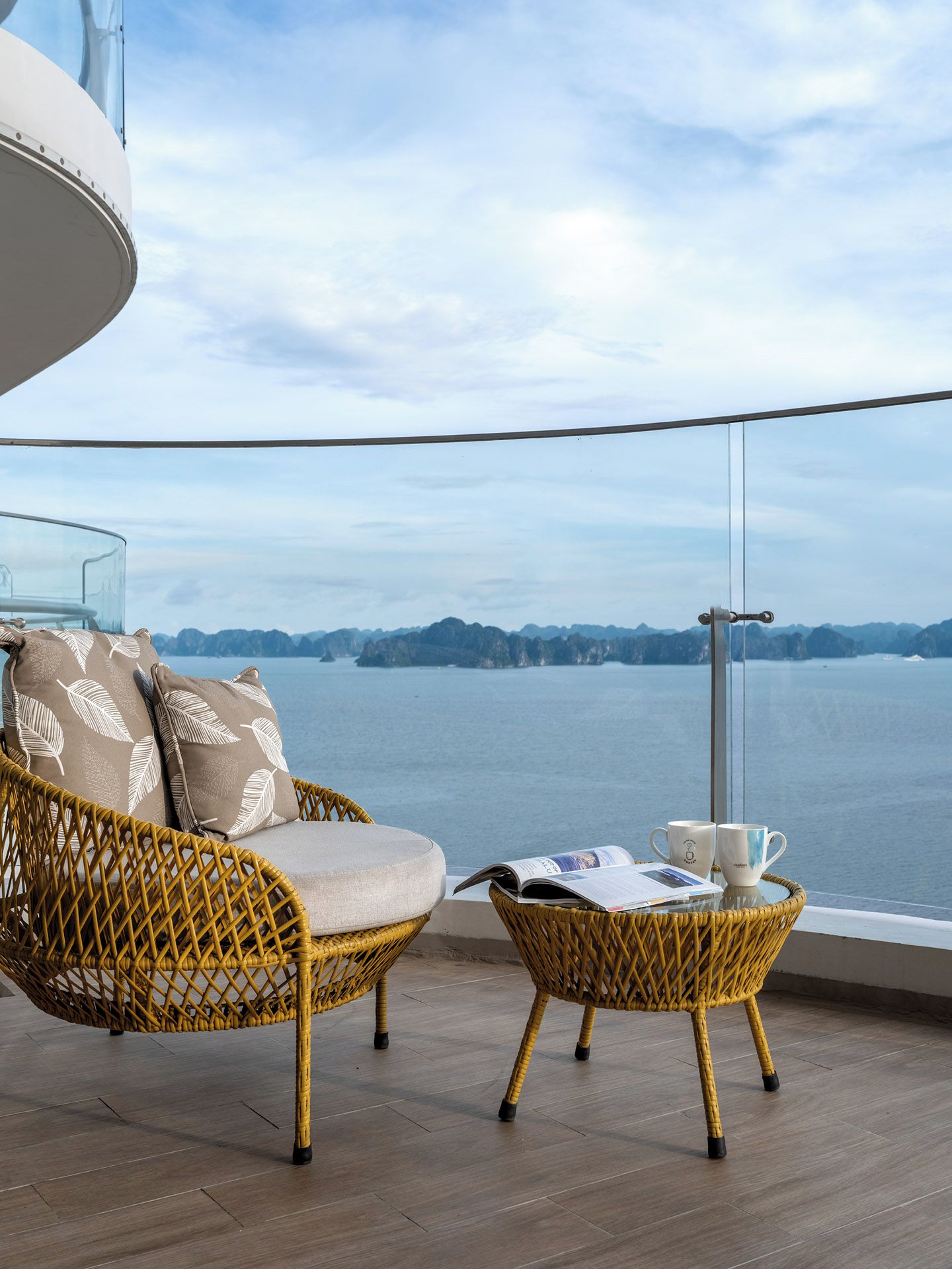 Ein Balkon mit Korbmöbeln, einem Glastisch und Blick auf das Wasser.