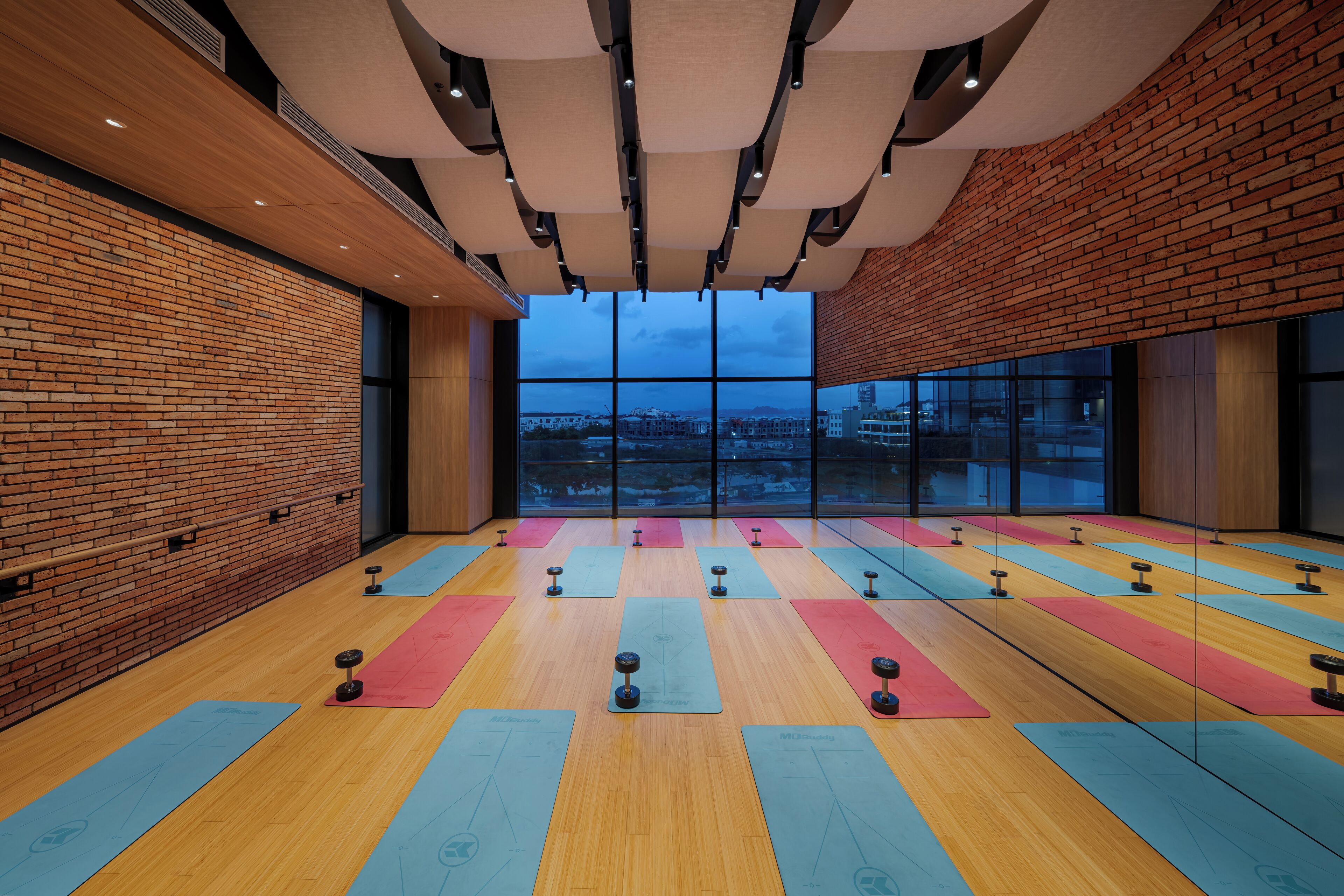 A spacious room with a wooden floor, large windows, and a brick wall.